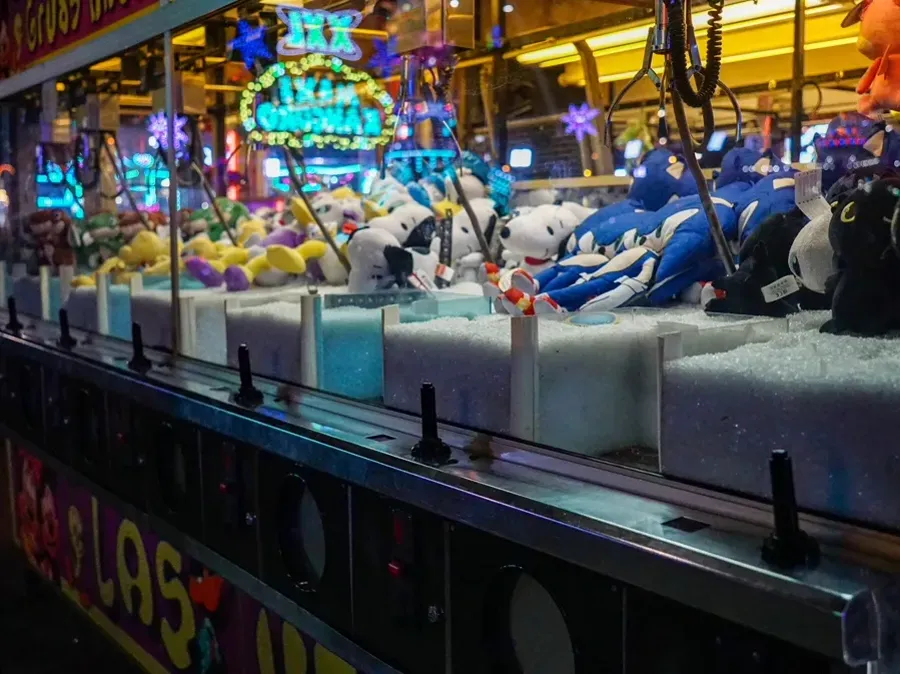 Fila di gru pesca-peluche illuminate al neon in una sala giochi